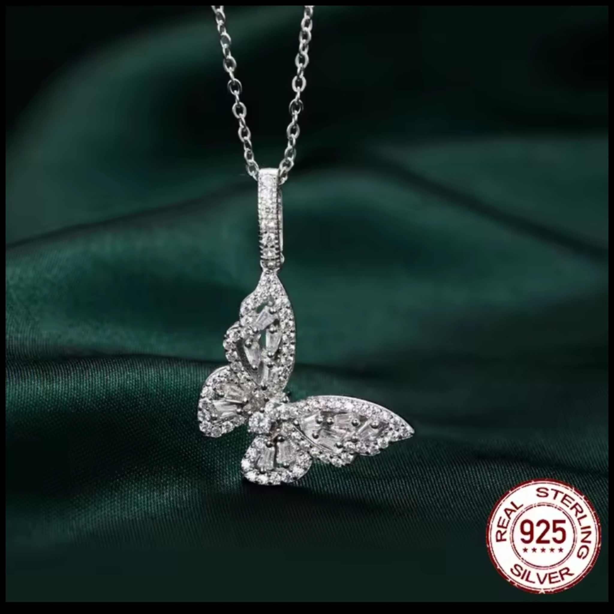 Silver butterfly pendant necklace on a dark green fabric background with 'Real Sterling Silver' 925 stamp.