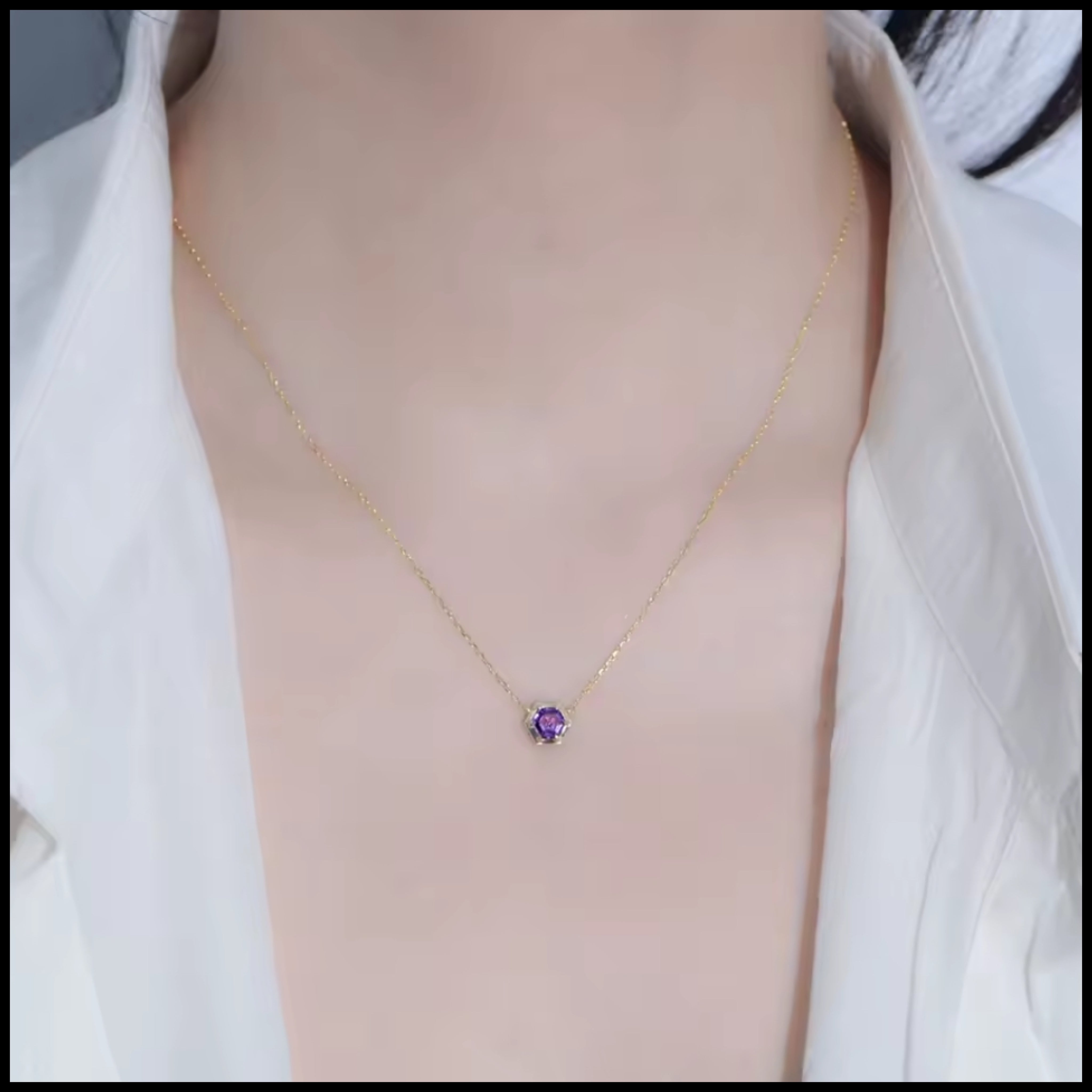 Necklace with a purple pendant worn by a person in a white shirt.
