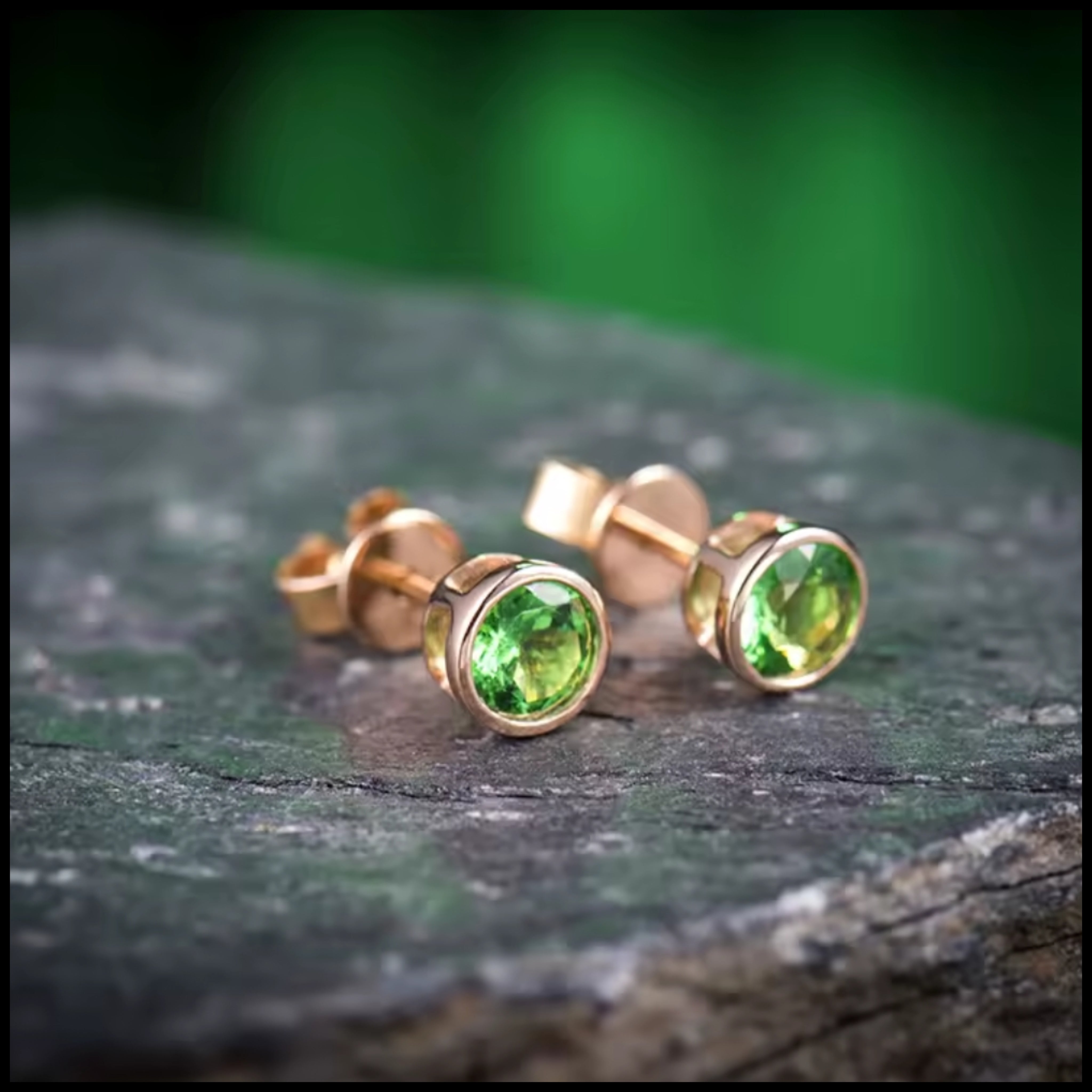 Tsavorite green stud earrings with round-cut gemstones set in 14k rose gold on stone surface