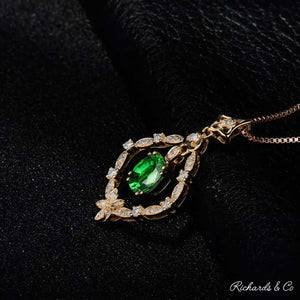 Close-up of Diamonds & Tsavorite pendant with oval green tsavorite garnet surrounded by sparkling white diamonds in 18K yellow gold setting on black background