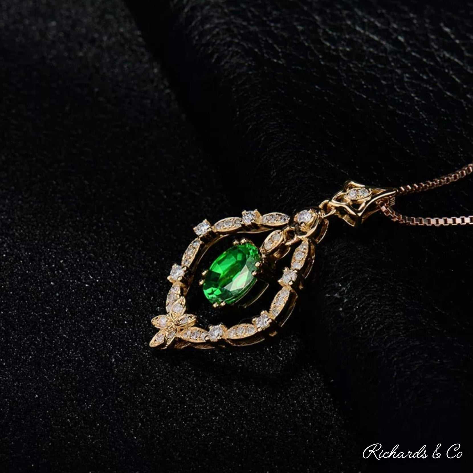 Close-up of Diamonds & Tsavorite pendant with oval green tsavorite garnet surrounded by sparkling white diamonds in 18K yellow gold setting on black background