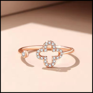 Rose gold four-leaf clover ring with cubic zirconia stones and adjustable band on beige background