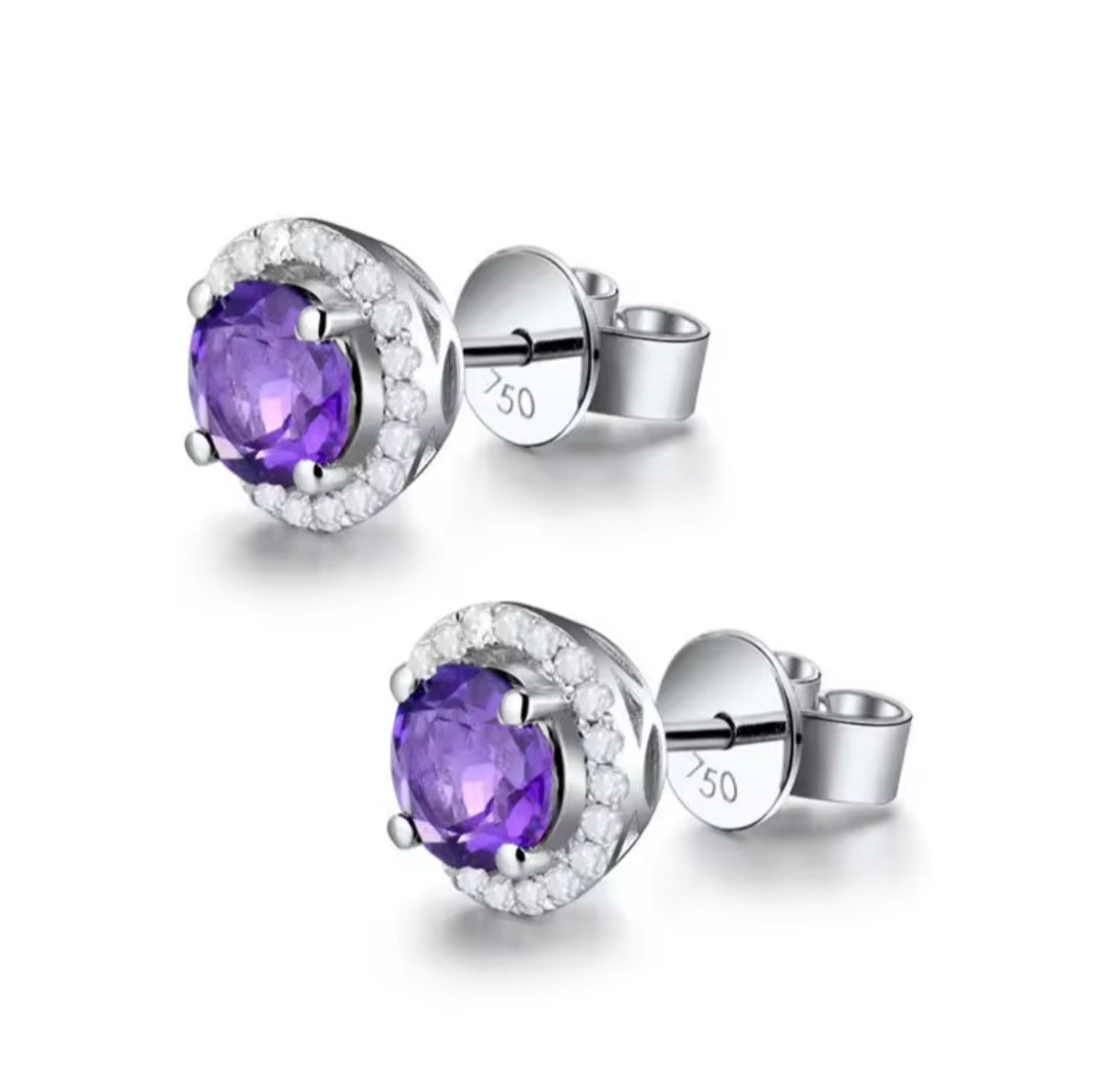 A pair of silver stud earrings featuring oval-cut purple amethyst centers surrounded by a halo of small clear diamond stones, shown on a clean white background.