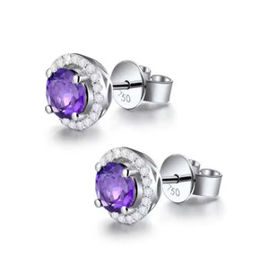 A pair of silver stud earrings featuring oval-cut purple amethyst centers surrounded by a halo of small clear diamond stones, shown on a clean white background.