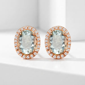 A pair of oval stud earrings featuring large light green amethyst centre stones surrounded by a halo of small clear natural diamond stones in rose gold settings, displayed on a clean white surface.