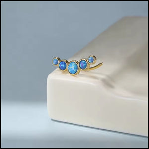 Gold earrings with blue gemstones on a light grey background