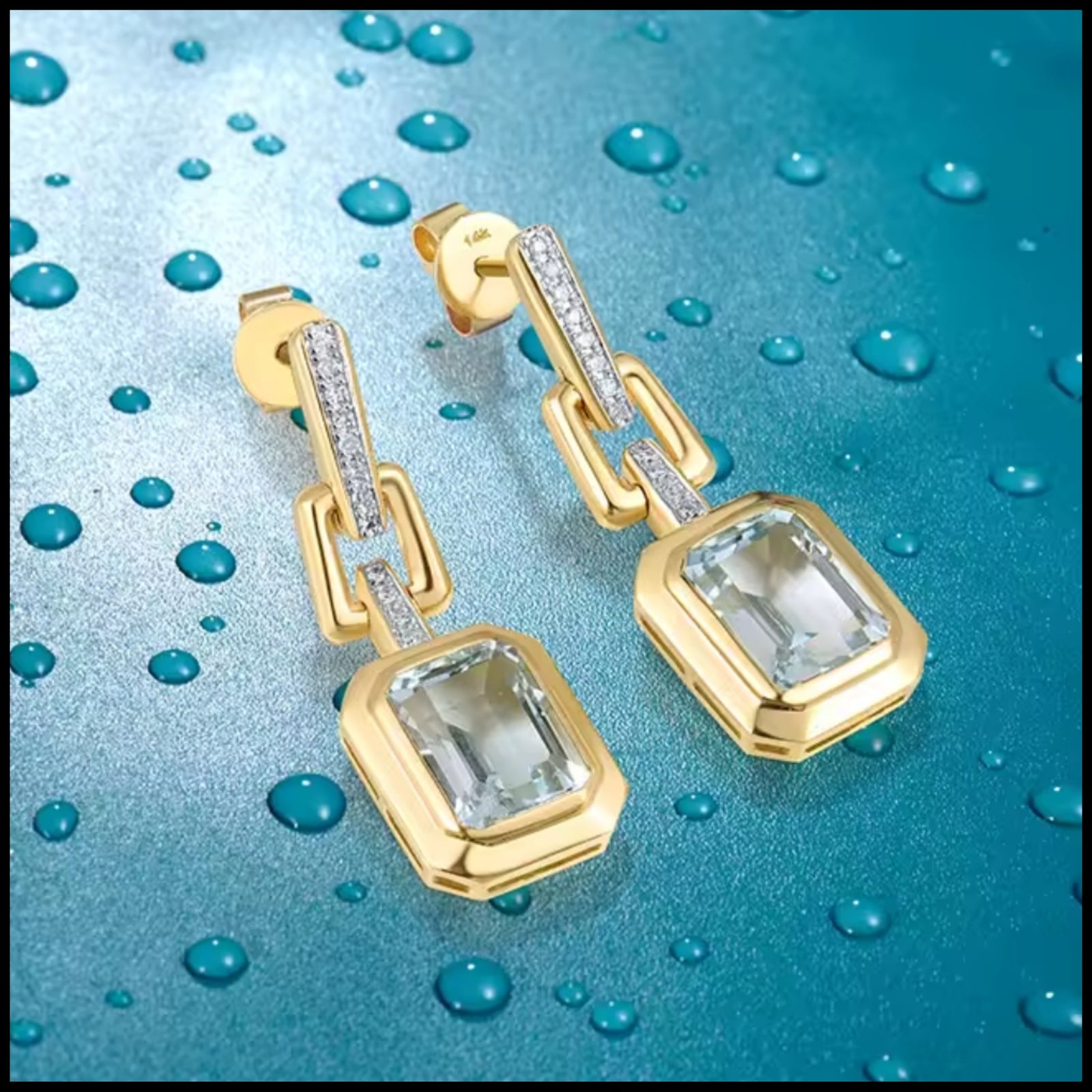 Gold earrings with clear gemstones on a blue water droplet background