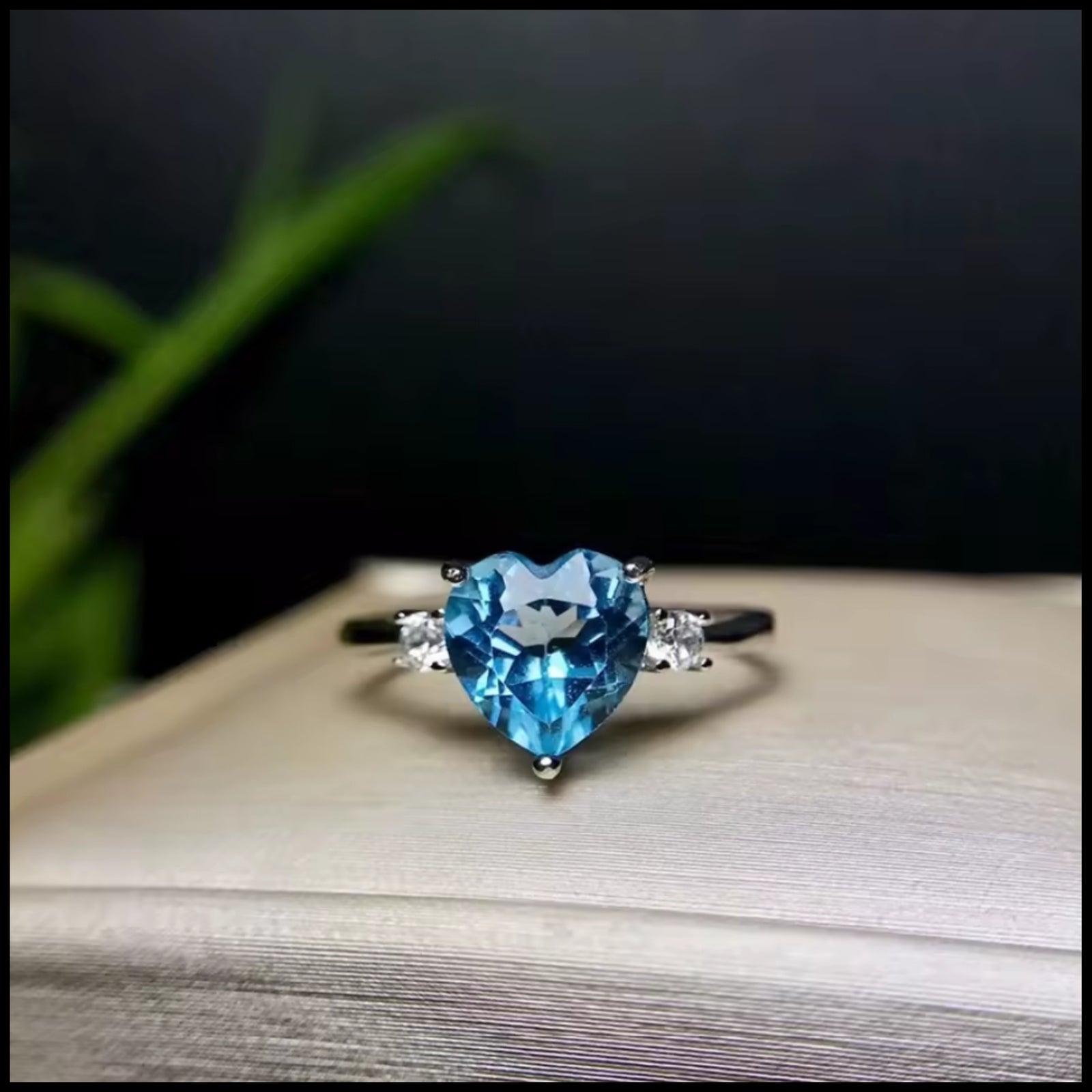 Heart-shaped blue topaz gemstone ring on a wooden surface with a blurred background