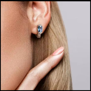 Close-up of a person wearing a blue gemstone earring with a neutral background