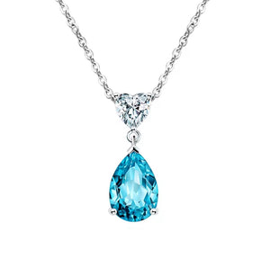 A silver pendant necklace featuring a faceted light blue teardrop-shaped gemstone and a small heart-shaped clear gemstone at the top, suspended from a delicate silver chain against a solid white background.