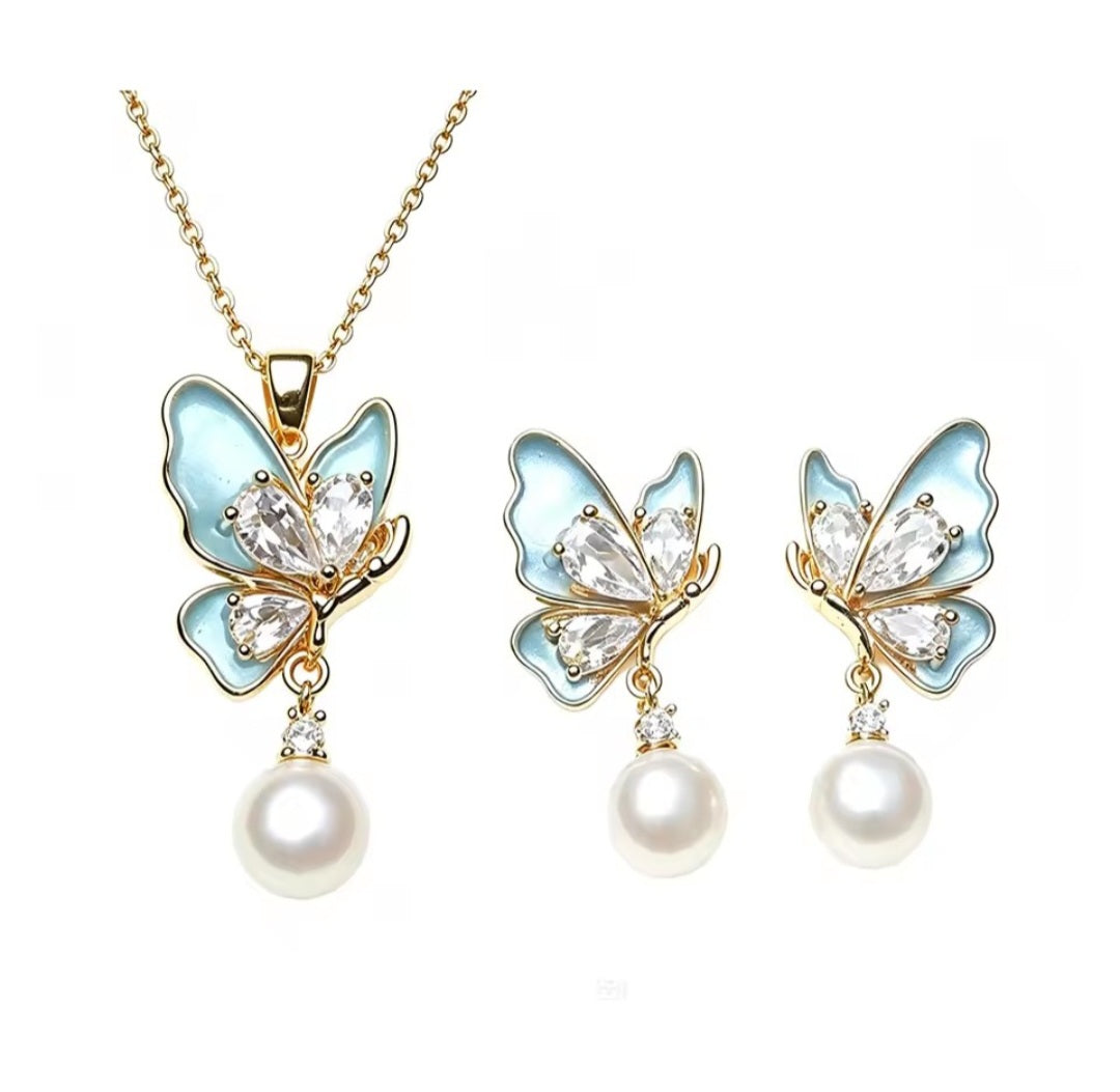 Gold-tone butterfly jewellery set with light blue enamel, clear rhinestones, and dangling white pearls, shown as a necklace and matching earrings on a white background.