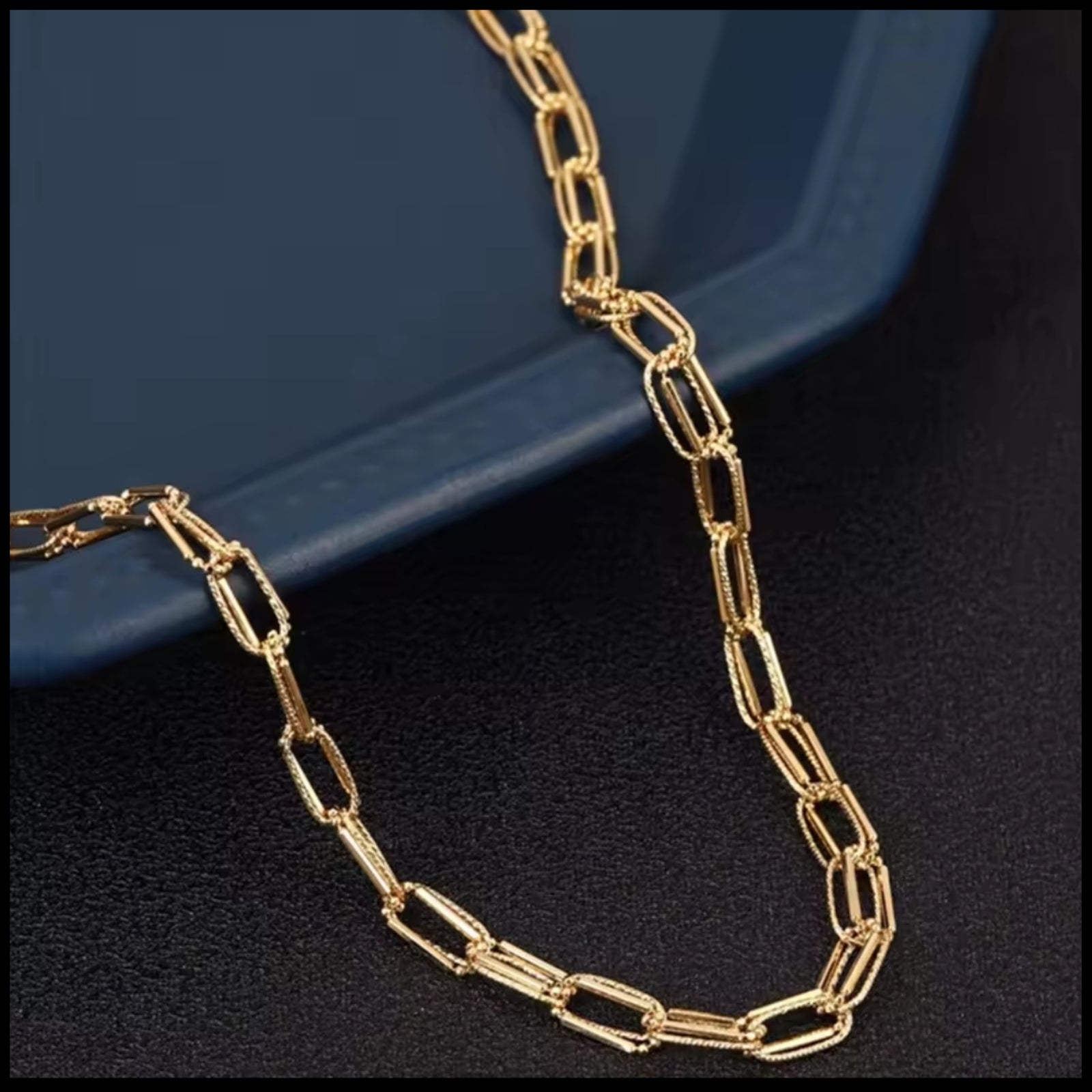 Gold chain necklace on a dark surface with a blue background