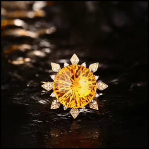 A yellow gold ring featuring a large citrine gemstone surrounded by smaller diamonds, set in a sunburst design.