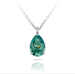 A pear-cut cyan blue gemstone pendant necklace in a silver setting on a delicate silver chain, shown against a white background with a soft reflection below.