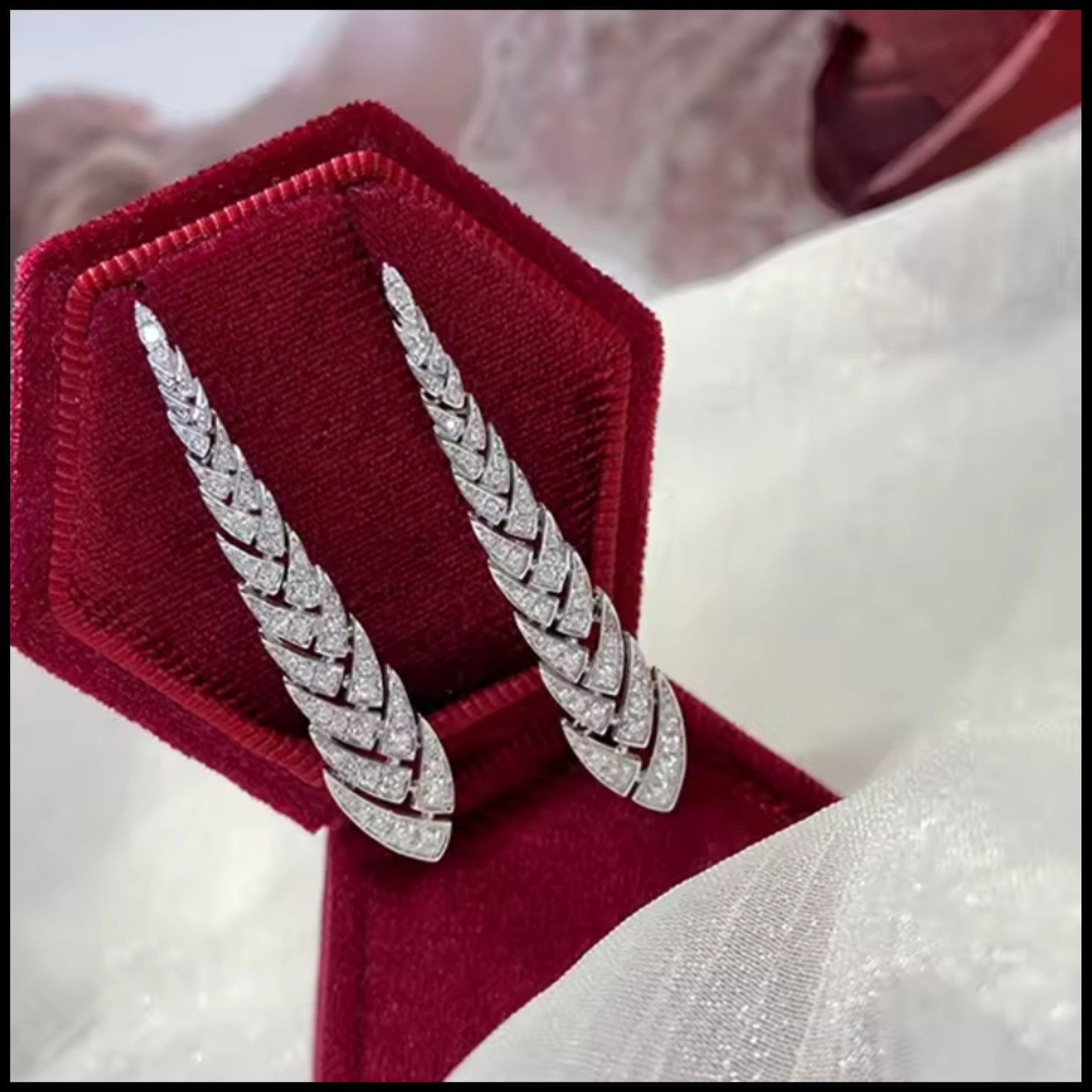 Silver feather-shaped earrings on a red velvet stand with a white fabric background
