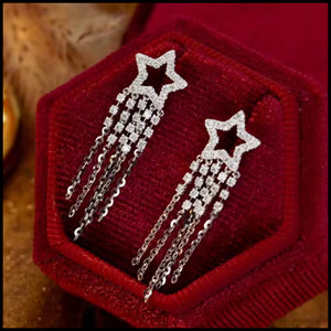 Star-shaped earrings with chain details on a red velvet stand.