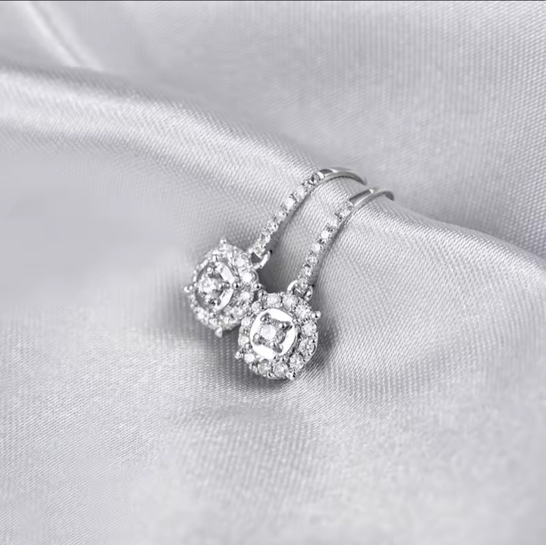 A pair of diamond halo earrings with clear round-cut diamond stones, displayed on draped satin fabric.