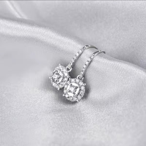 A pair of diamond halo earrings with clear round-cut diamond stones, displayed on draped satin fabric.