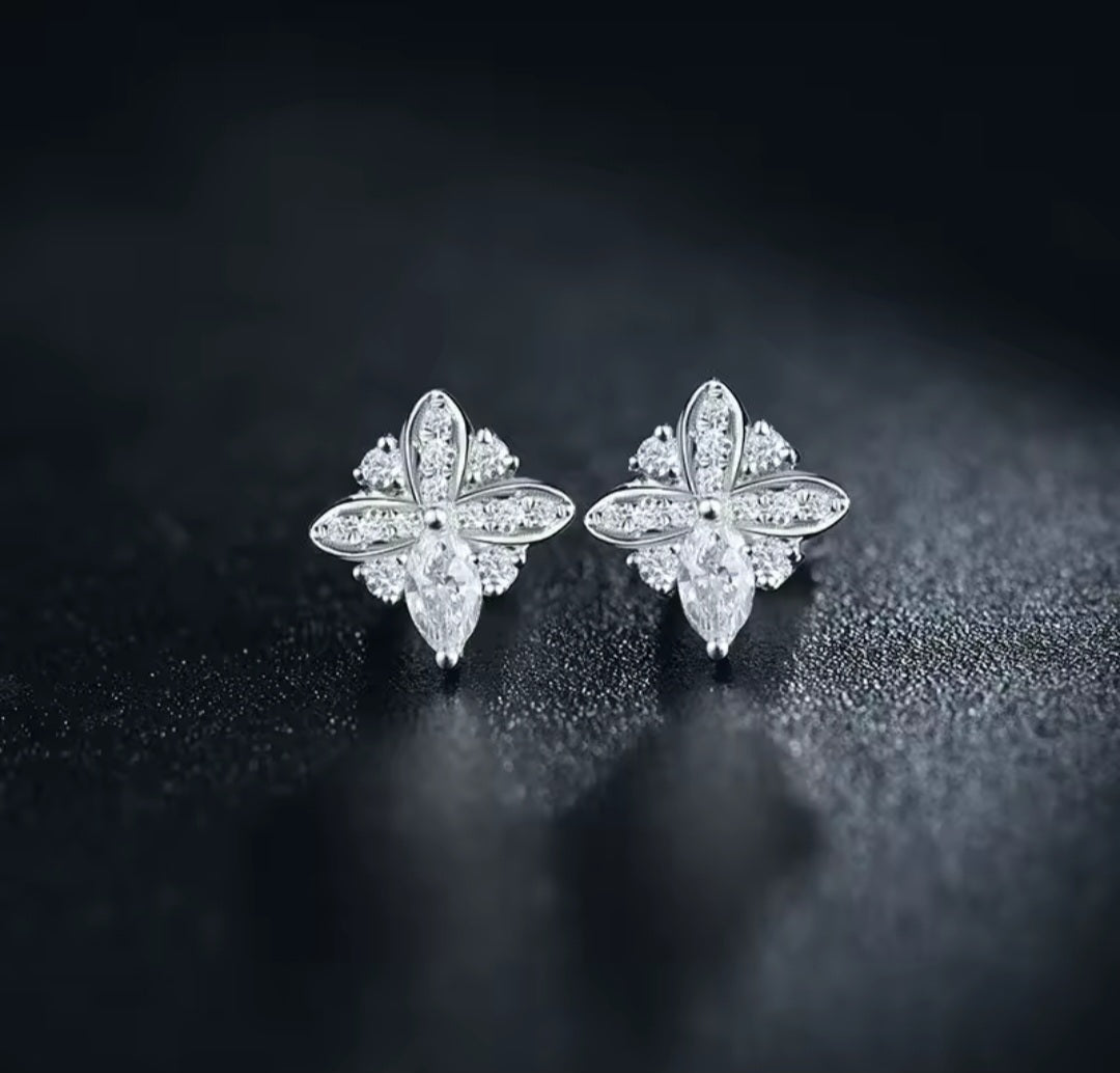 A pair of white gold flower-shaped stud earrings set with clear marquise and round natural diamond gemstones, displayed on a dark textured surface.
