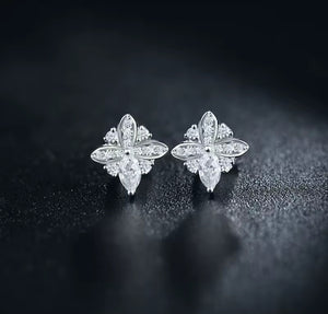 A pair of white gold flower-shaped stud earrings set with clear marquise and round natural diamond gemstones, displayed on a dark textured surface.
