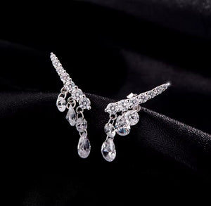 A pair of silver-tone drop earrings with clear teardrop and round crystals, displayed on a black fabric background.