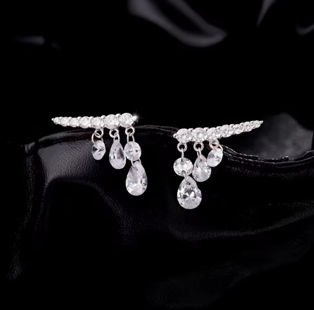 A pair of silver-toned teardrop-shaped earrings adorned with clear teardrop crystals and small clear stones along the top bar, displayed on a black satin surface.
