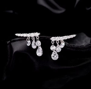 A pair of silver-toned teardrop-shaped earrings adorned with clear teardrop crystals and small clear stones along the top bar, displayed on a black satin surface.
