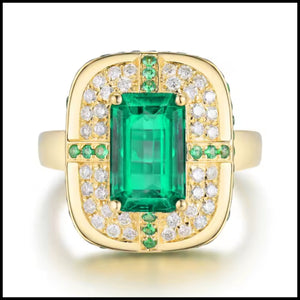 Gold ring with a green emerald gemstone and smaller diamonds on a white background