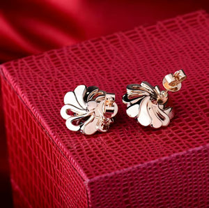 A pair of 18k rose gold fan-shaped earrings and natural emerald with a polished finish, displayed on a textured red gift box.