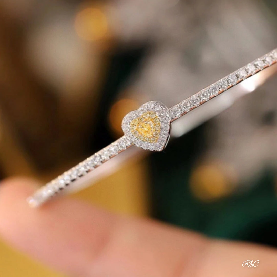 A hand holding a yellow diamond heart-shaped bracelet with smaller white diamonds set in a white gold band.