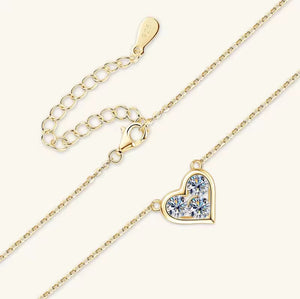 Gold chain necklace with a heart-shaped pendant set with clear stones, shown on a light cream background with its extender chain.