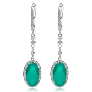 A pair of silver drop earrings featuring oval emerald-cut green gemstones surrounded by small clear stones, with leverback hooks and diamond-shaped accents, shown on a white background.