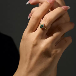 Hand wearing a gold ring with a green gemstone on a dark background