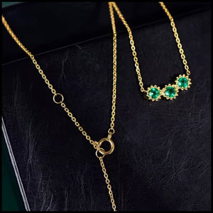 Gold necklace with green gemstones on a black surface