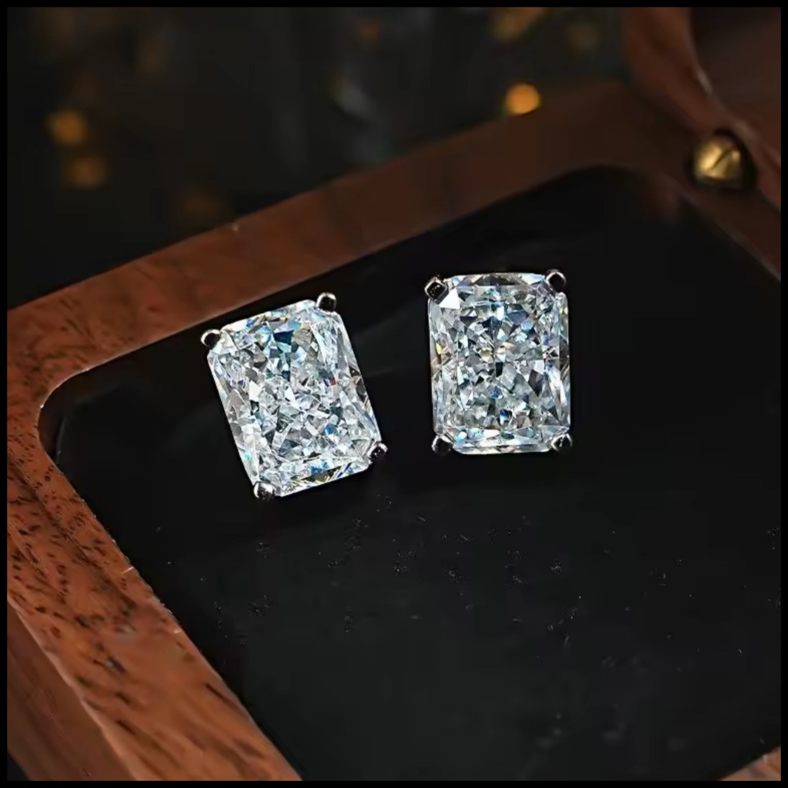 Pair of diamond earrings on a dark surface with a wooden frame.