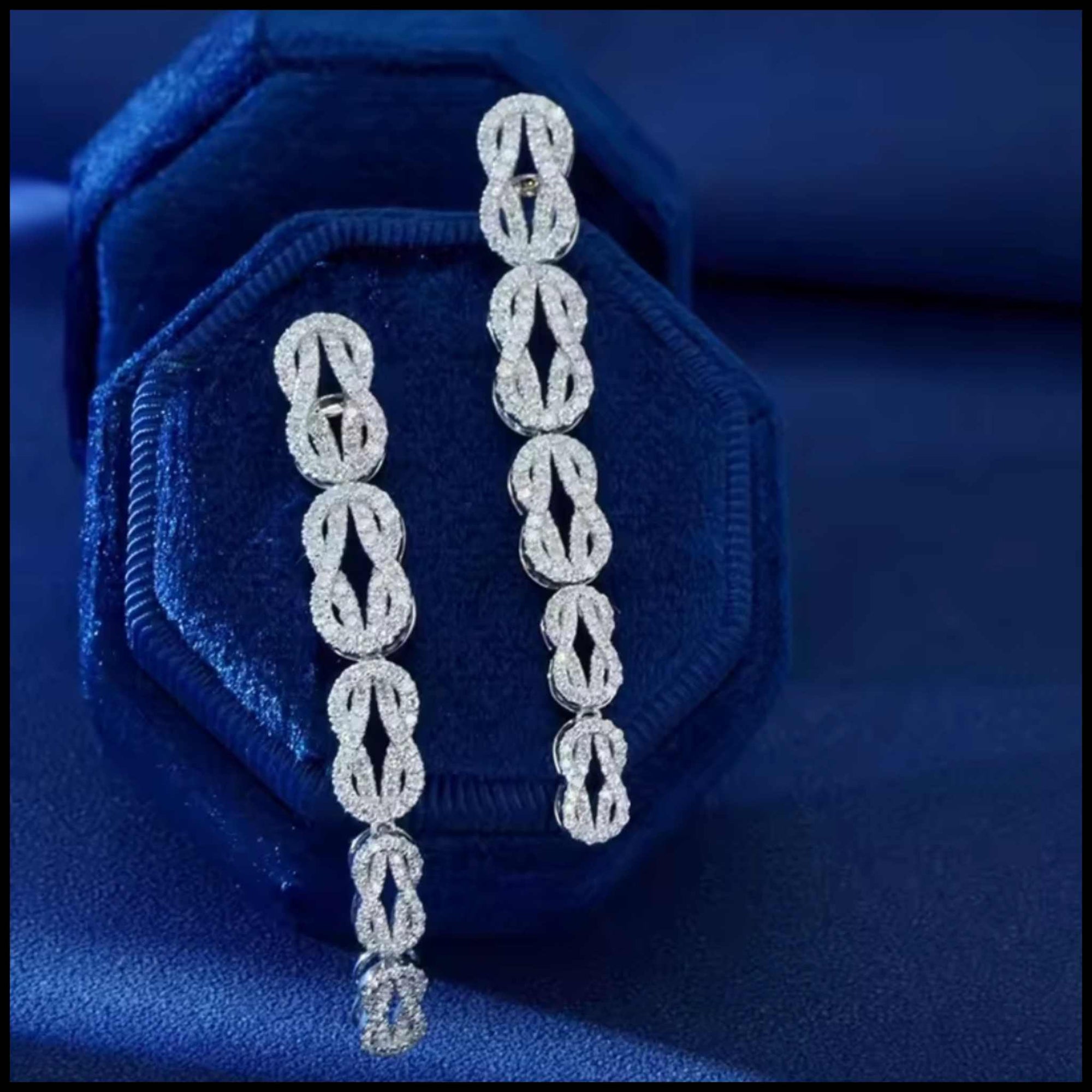 Pair of diamond chain earrings on a blue velvet cushion