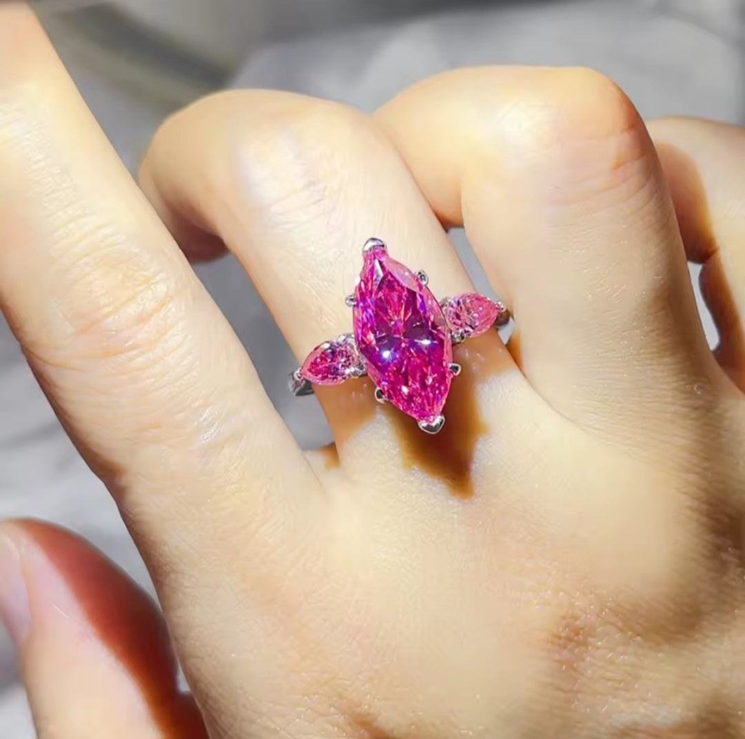 A close-up of a hand wearing a silver ring with a large marquise-cut pink gemstone and smaller pink stones on the sides.