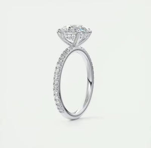 A silver moissanite ring featuring a large marquise-cut centre stone in a four-prong setting, with a pavé band of small round diamonds, shown on a light grey background.