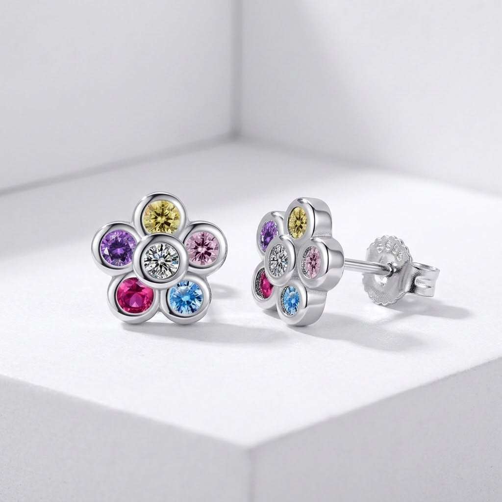 A pair of silver flower-shaped stud earrings with multiple colourful gemstones, displayed on a clean white geometric surface.