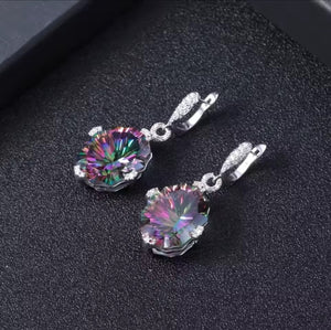 A pair of silver-toned drop earrings with large round iridescent gemstones, displayed on a textured black surface.