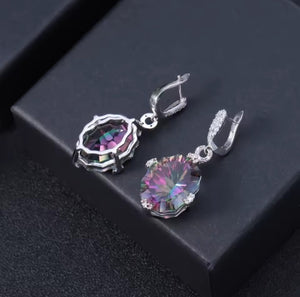A pair of silver-toned drop earrings with large, round, iridescent purple and green gemstones, displayed on a black textured surface.