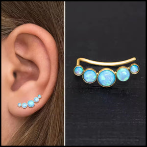 Gold and blue opal gemstone earrings worn on an ear with a black background