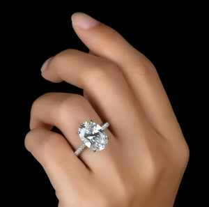 A close-up of a hand wearing a silver-toned ring with a large round brilliant-cut clear gemstone, set against a solid black background.