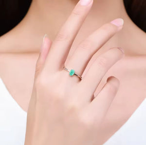 A close-up of a person's hand wearing a delicate silver ring with a small, vibrant green marquise-cut gemstone.