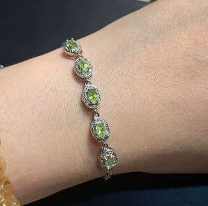 A close-up of a silver-toned bracelet with five oval green peridot gemstones, worn on a person's wrist.