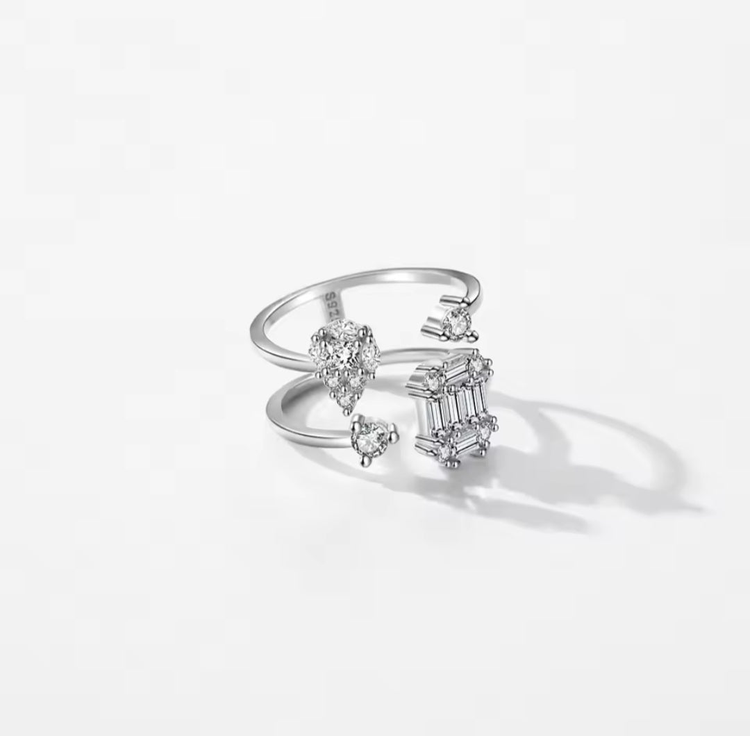 A silver open ring featuring multiple diamond-cut and baguette gemstone clusters, photographed on a clean white background with a soft shadow.