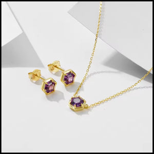 Gold necklace and earrings with purple gemstones on a white background