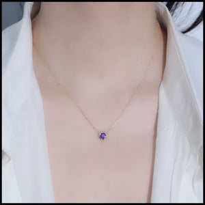 Necklace with a purple pendant worn by a person in a white shirt.