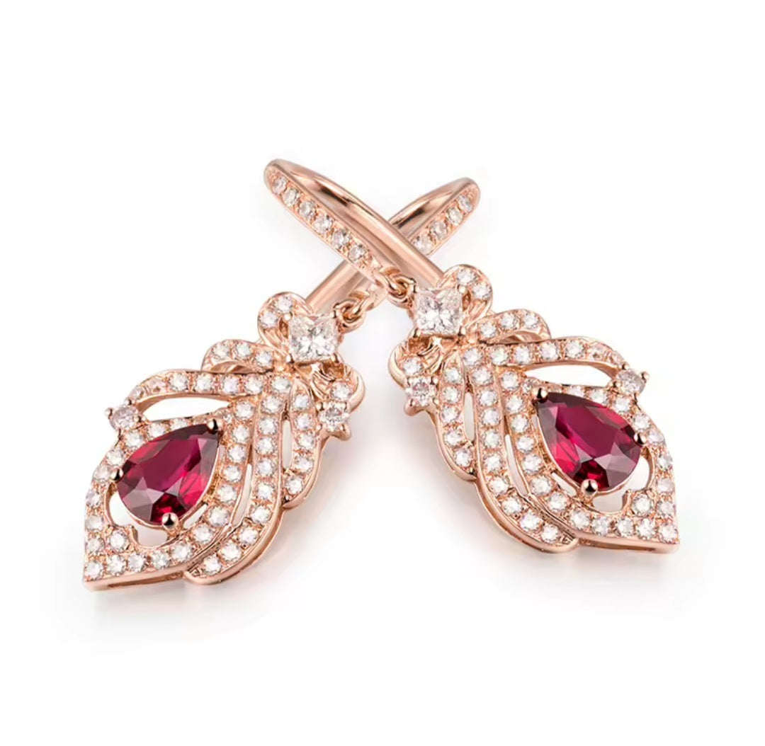 A pair of rose gold drop earrings featuring teardrop-shaped deep red gemstones surrounded by pavé-set clear stones, shown on a clean white background.