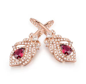 A pair of rose gold drop earrings featuring teardrop-shaped deep red gemstones surrounded by pavé-set clear stones, shown on a clean white background.